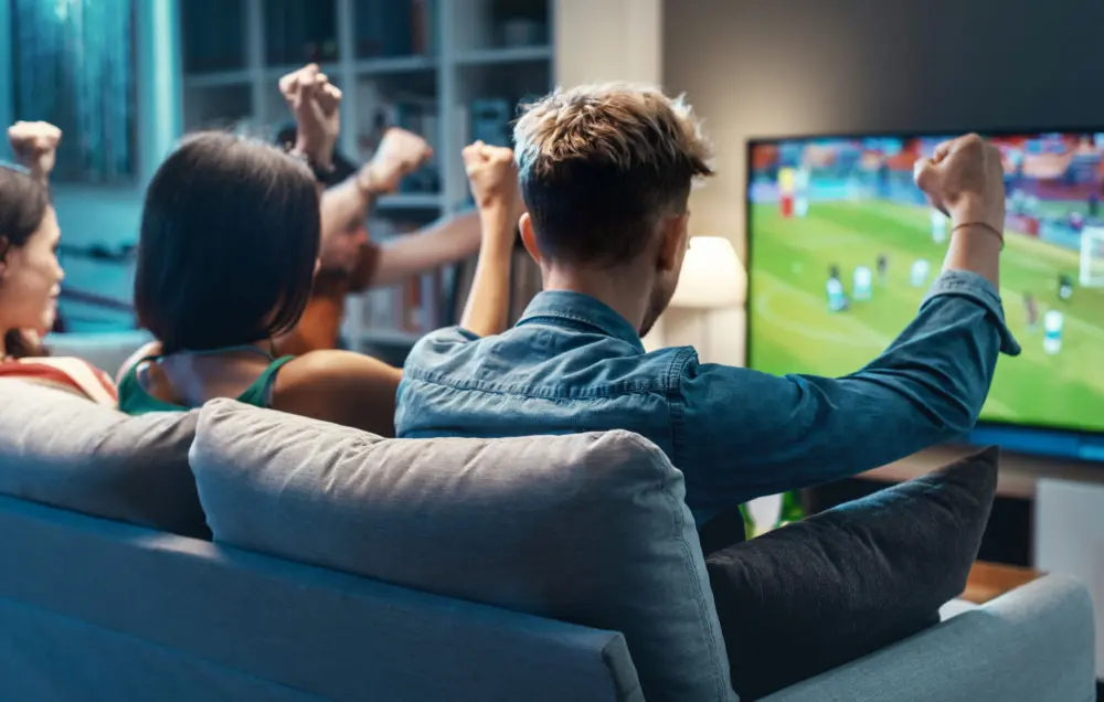 Friends watching a sporting event together and discussing predictions, reflecting the social nature of sports betting.