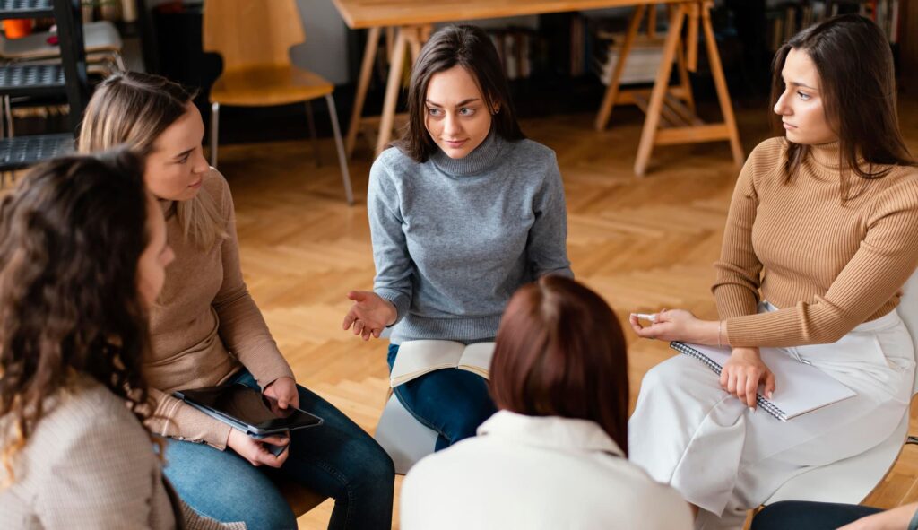Support group of diverse people sitting in circle listening to someone speak