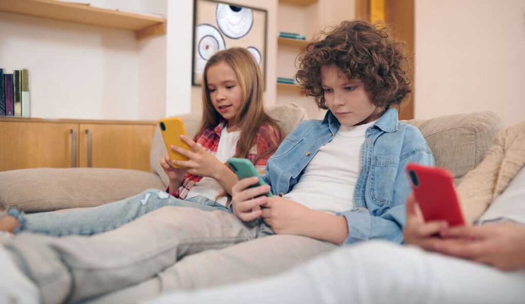 Two teens sitting on sofa looking at their cell phones